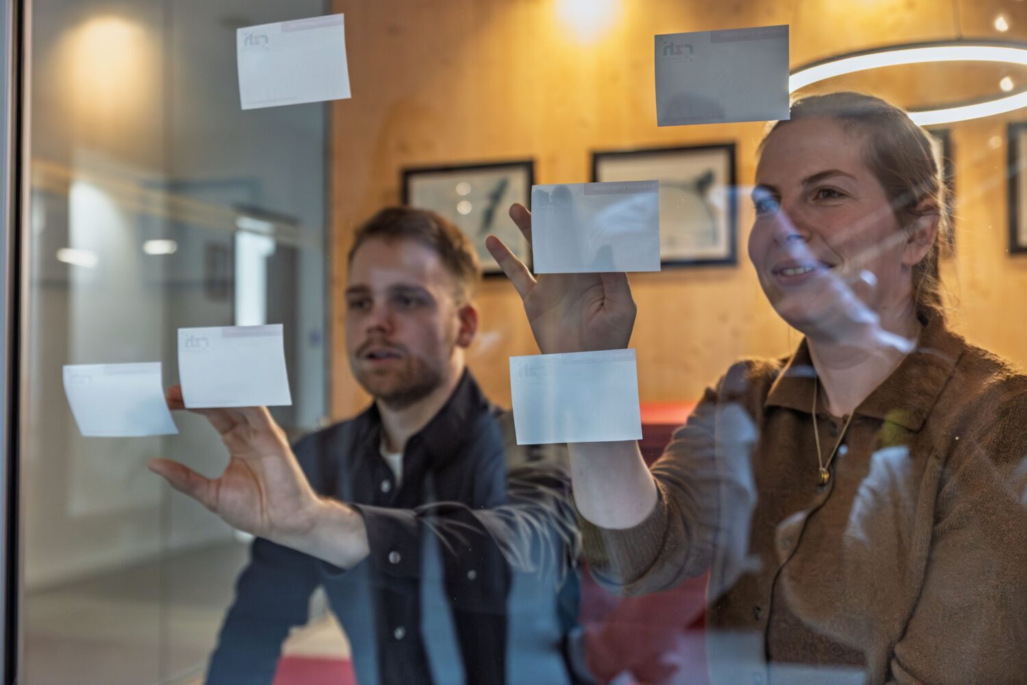 Eine Frau und ein Mann haben Post-it an einer Glasscheibe platziert.