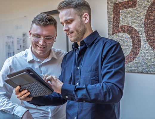 Foto von zwei jungen Männern die auf ein Tablet schauen.