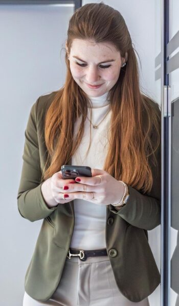 Eine Frau im Bürogebäude schaut auf ihr Handy.