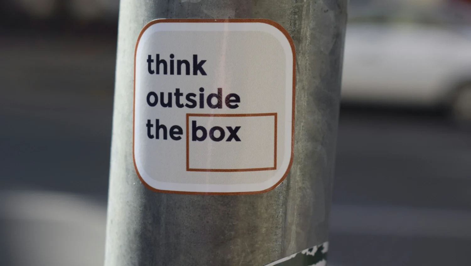 Grauer Laternenpfahl mit einem Sticker auf den der Text think outside the box steht. Das Bild soll für Guerilla Recruiting stehen.